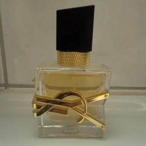 Yves Saint Laurent Libre parfym - 30ml, Snygg och lyxig parfymflaska från Yves Saint Laurent, Libre. Flaskan är genomskinlig med guldiga detaljer och svart asymmetrisk kork. Doften har inslag av vit blomma, citrus, lavendel och vanilj. Perfekt för dig som gillar eleganta och moderna dofter.