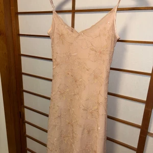Champagnefärgad blommig långklänning - Superfin långklänning i champagne/ljusrosa färg. Paljetter och broderade blommor, från stradivarious storlek xs. Använd en gång. Finns ett par trådar som sticker ut men kan klippas bort/syns annars inte