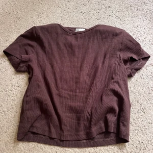 Brun ribbad kortärmad topp - En enkel och stilren brun ribbad topp med korta ärmar. Toppen har en rund halsringning och är tillverkad i ett mjukt, stretchigt material som sitter skönt på kroppen. Perfekt att matcha med jeans eller kjol för en avslappnad look.