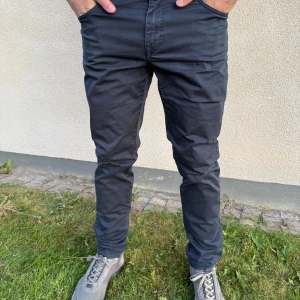 Svarta J.Lindeberg chinos i slim fit - Snygga svarta chinos med slim passform och klassiska fickor både fram och bak. Byxorna har en stilren look och är tillverkade i ett mjukt bomullsmaterial med lite stretch för extra komfort. Perfekta för dig som gillar en clean och modern stil.