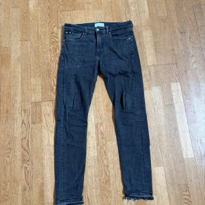 Svarta jeans Calvin Klein - Snygga svarta skinny jeans från Calvin Klein med klassisk femficksdesign och råa benslut. Jeansen har en smal passform och är tillverkade i stretchigt denim för extra komfort. Perfekta för dig som gillar en stilren och modern look.