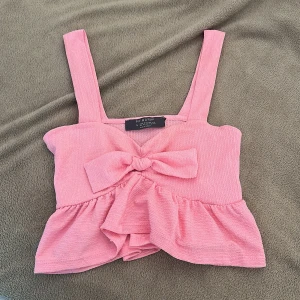 Rosa linnetopp med rosett - Supersöt rosa linnetopp från Primark med breda axelband, stor rosett framtill och volang nertill. Toppen är ärmlös och har en croppad passform som ger en trendig vibe. Perfekt för sommaren💗