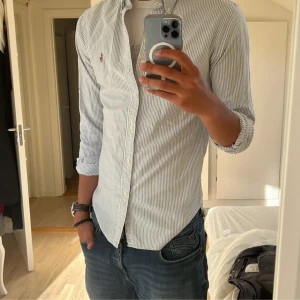 Ralph Lauren Skjorta (pris diskuterbart) - !!NY SKICK !!Säljer en klassisk blå randig  skjorta från Ralph Lauren i storlek S SLIMFIT med button-down krage och broderad logga på bröstet. Skjortan har lång ärm, knappar framtill och är gjord i mjuk bomull. Perfekt för dig som gillar stilrena och snygga plagg.