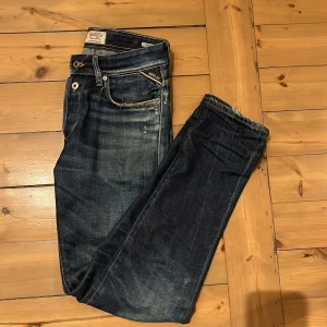 Replay jeans  - Snygga Replay RBJ.901 jeans i mörkblå tvätt med slitna detaljer och klassiska kontrastsömmar. Modellen har fem fickor, knappgylf och Replay-logga på myntfickan. Perfekta för dig som gillar en cool och avslappnad stil.