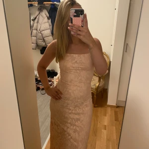 Ljusbeige/rosa långklänning  - Supersnygg långklänning i ljusbeige/rosa färg med blommigt mönster och smala axelband. Klänningen har figurnära passform och raka linjer, perfekt för dig som vill ha en elegant och stilren look. Materialet känns mjukt och följsamt.