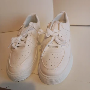 Helvita sneakers med chunky sula - Snygga helvita sneakers med chunky platt sula och klassisk snörning. Ovandelen är i syntet med perforerade detaljer för extra stilpoäng. Perfekta för dig som gillar en clean och fräsch look till vardagsoutfiten.