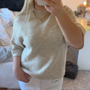 Beige stickad tröja med kort ärm - Supermjuk beige stickad tröja med kortare ärmar och rund halsringning. Enkel och stilren modell som är lätt att matcha till olika outfits. Perfekt för lager-på-lager och funkar året runt. Materialet känns skönt mot huden och ger en avslappnad vibe.