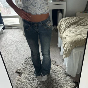 Dirty Free jeans med fjärilsdetaljer - Säljer ett par blå jeans från Dirty Free med låg midja och bootcut. Jeansen har snygga silvriga nitar och strass på fickorna samt en stor glittrig fjäril på baksidan. Perfekt för dig som gillar detaljer och vill sticka ut lite extra. Det saknats en knapp på baksidan av jeansen visat på bilden men det går väldigt enkelt att laga. 💖