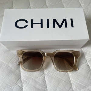  solglasögon från CHIMI - Ecru 04 - Snygga solglasögon från CHIMI med fyrkantig form och transparent beige båge. Glasen är mörka och ger en cool kontrast till den ljusa ramen. Kommer med originaletui och box. Perfekta för att lyfta din stil i sommar!