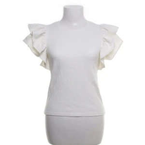 Vit ribbad topp med volangärmar - Säljer en söt vit ribbad topp från Zara med volangdetaljer på ärmarna. Perfekt för en stilren look. Toppen har en rund halsringning och är i ett mjukt material.