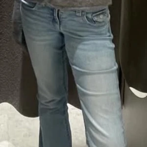 Ljusblå bootcut jeans med fickdetalj - Säljer ett par ljusblå jeans med bootcut passform och snygga fickdetaljer bak med knapp. Jeansen har låg midja och är tillverkade i mjukt denim. 