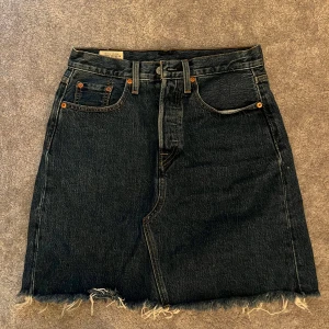 Levi's jeanskjol med fransig kant - Mörkblå jeanskjol från Levi's Premium med klassiska fickor, bälteshällor och rå, fransig nederkant. Snygg och enkel modell som är lätt att matcha till olika stilar. Perfekt för dig som gillar en avslappnad vibe.