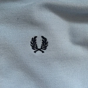 Ljusblå Fred Perry pikétröja M - Snygg ljusblå slim fit pikétröja från Fred Perry med klassisk svart logga broderad på bröstet. Tröjan har svarta ränder på krage och ärmslut, korta ärmar och är gjord i bomullspiké.  Nypris 1000kr (priset kan diskuteras)