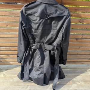Svart trenchcoat från Burberry - Snygg svart trenchcoat från Burberry med klassisk design. Jackan har ett bälte i midjan för en justerbar passform. Perfekt för en stilren look. Används bara en handfull gånger. i perfekt skick Försäljningsorsak till graviditet nypris:24000:- Pris kan diskuteras vid snabbt köp