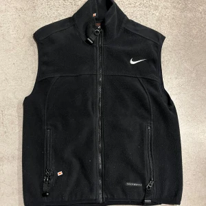 Svart fleeceväst Nike ACG - Vintage Nike ACG väst. Köpt beggad men satt för tajt. perfekt nu till våren. Den har två defekter där den gått sönder lite (bild3/4), därav det låga priset. Köp fler via ”köp nu funktionen” :) 