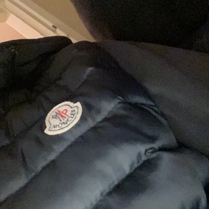 Svart pufferjacka från Moncler - Säljer en snygg svart pufferjacka från Moncler. Jackan har en quiltad design och är perfekt för kyligare väder. Den har en klassisk Moncler-logga på bröstet. Perfekt för dig som vill hålla stilen i vinter! 🖤