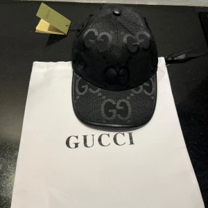 Svart keps från Gucci - Snygg svart keps från Gucci med det ikoniska GG-mönstret. Kepsen har en klassisk design med rundad skärm och justerbar passform. Perfekt för att ge din outfit en lyxig touch.