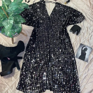 Svart paljettklänning från Lindex - Snygg svart klänning täckt med glittriga paljetter. Den har en v-ringad design och korta ärmar. Perfekt för en festlig kväll med sitt iögonfallande utseende. Klänningen har även en knytning i ryggen för extra detalj. storlek L/XL!  En klänning som kommer få dig att skina ✨  Ny! Använd en gång!  Nypris 799 :- Öppen för prisförslag!