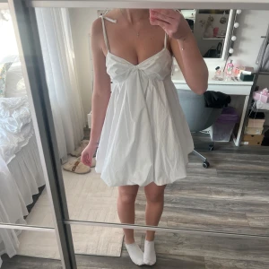 Vit kortklänning med knytband - Säljer en söt vit kortklänning från NA-KD med smala axelband och knytband. Klänningen har en luftig passform och en v-ringad design framtill. Perfekt för studenten!💕 Aldrig använd och har prislapppen kvar🌸Ny pris 600kr