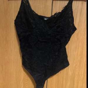 Svart spetsbody från bubbleroom - Snygg svart spetsbody från bubbleroom med v-ringning och smala axelband. Perfekt för en kväll ute eller som en del av en lager-på-lager-look. Den har en elegant och sexig design som framhäver figuren.