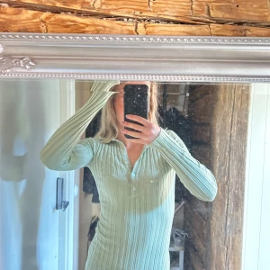 Ljusgrön ribbad klänning - Säljer en stilren ljusgrön ribbad klänning med lång ärm och knappar framtill. Perfekt för en avslappnad eller uppklädd look. Passar bra till både vardag och speciella tillfällen.