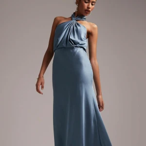 Blå långklänning från ASOS Edition - Elegant blå långklänning från ASOS Edition med en unik halterneck-design. Klänningen har en vacker drapering framtill och är tillverkad i ett mjukt, glansigt material som ger en lyxig känsla. Perfekt för speciella tillfällen.