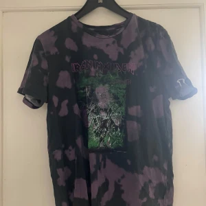 Svart och lila Iron Maiden t-shirt - Säljer en cool svart och lila t-shirt med Iron Maiden-tryck. T-shirten har ett unikt mönster och korta ärmar, perfekt för fans av bandet. Passar bra till vardags eller konsert!