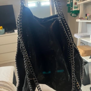 Svart axelväska med kedjedetaljer - Snygg svart axelväska med kedjedetaljer längs kanterna. Väskan har en dragkedja på baksidan för extra förvaring💞