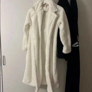 Vit teddyjacka - Säljer en supermysig vit teddyjacka som är perfekt för kyliga dagar. Jackan har en lång och fluffig design med långa ärmar och en klassisk krage. Den är både stilren och bekväm, vilket gör den till ett måste i garderoben. Perfekt för att hålla sig varm och snygg under vintern.