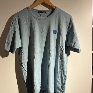 Ljusblå t-shirt från Acne Studios - Säljer en stilren ljusblå t-shirt från Acne Studios. Den har en rund halsringning och ett diskret märke på bröstet. Perfekt för en avslappnad look.