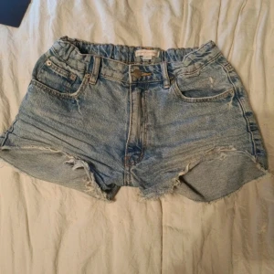 Lågmidjade jeansshorts med fransar - Säljer ett par coola blå jeansshorts med fransiga kanter. De har en klassisk femficksdesign och en knappgylf. Perfekta för en avslappnad stil. Lågmidjade och justerbar midja.