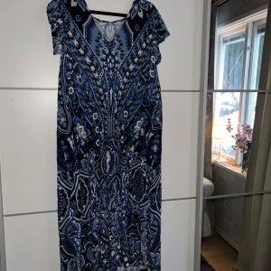 Blå mönstrad klänning - Snygg blå klänning med ett detaljerat mönster i olika nyanser av blått och vitt. Klänningen har korta ärmar och en bekväm passform. Perfekt för en avslappnad dag eller en speciell kväll. Mönstret ger en unik och stilfull look.