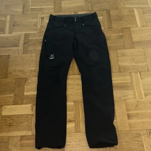 Svarta byxor från Haglöfs - Snygga svarta byxor från Haglöfs med knappar framtill. Perfekta för utomhusaktiviteter med en stilren design. Byxorna har en normal passform och är tillverkade i ett slitstarkt material.