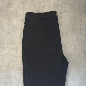 Svarta jeansbyxor från H&M - Snygga svarta jeansbyxor från H&M med låg midja och dragkedja. Perfekta för en stilren look. Byxorna har en klassisk design med utsvängda ben och en enkel bakficka.