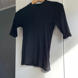 Svart ribbad topp från Lindex - Säljer en stilren svart ribbad topp från Lindex. Toppen har en hög hals och trekvartsärmar, samt att den sitter tight. Skriv för fler bilder/frågor🫶🏻
