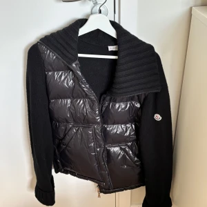 Vår jacka från Moncler - Snygg svart vårjacka från Moncler med en kombination av glansigt och stickat material. Jackan har en dragkedja framtill och en ribbad krage. Har ej kvitto där av priset!🌟