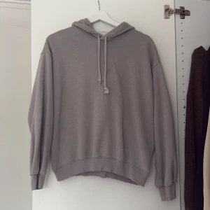 Grå hoodie från H&M - Säljer en stilren grå hoodie från H&M. Den har en klassisk design och ribbade muddar vid ärmslut och nederkant. Perfekt för en avslappnad look.