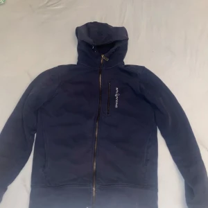 Svart fleecejacka från Peak Performance - Säljer en svart fleecejacka från Peak Performance med dragkedja och huva. Jackan har långa ärmar och en stilren design, perfekt för kyliga dagar. Den är mjuk och bekväm att bära.