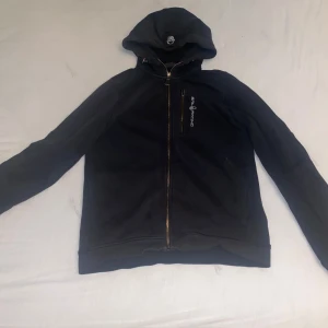 Svart huvtröja från GASP - Säljer en svart huvtröja från GASP med dragkedja och tryckt logga på bröstet. Tröjan har långa ärmar och en bekväm huva. Perfekt för träning eller en avslappnad dag.