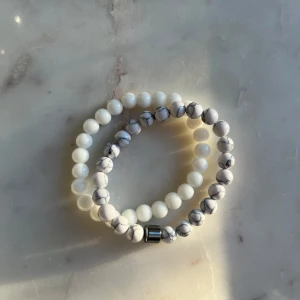 Vita och marmorerade armband - Två elastiska armband med vita och marmorerade pärlor. Det ena armbandet har helt vita pärlor medan det andra har en marmorerad design med en metallisk detalj. Perfekt för att mixa och matcha.