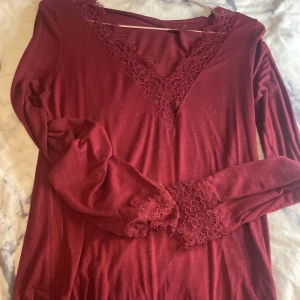 Vinröd långärmad topp från intimissimi - Säljer en elegant vinröd långärmad topp med v-ringning och spetsdetaljer vid hals och ärmslut. Perfekt för en stilren look. 💃