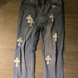 Chrome Hearts Jeans - Unika blå jeans dekorerade med vita korsdetaljer. Byxorna har en klassisk femficksdesign och en avslappnad passform. Perfekta för att ge din outfit en edgy touch.