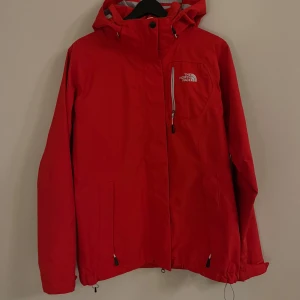 Röd jacka från The North Face - Säljer en snygg röd jacka från The North Face. Jackan har en dragkedja framtill och en justerbar huva. Perfekt för kyliga dagar med sin stilrena design och praktiska detaljer.