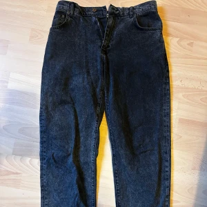 Svarta jeansbyxor - Snygga svarta jeansbyxor med en klassisk design. De har en rak passform och är tillverkade i ett robust denimtyg. Perfekta för en avslappnad stil. Lite slitna längs ner på vänster ben som man kan se på andra bilden.