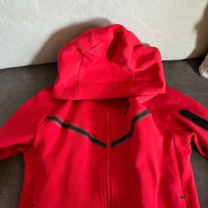 Röda mjukisbyxor från Nike - Snygga röda mjukisbyxor från Nike med elastisk midja och snörning. Byxorna har en avslappnad passform och är perfekta för en bekväm stil. Nike-loggan är tryckt på ena benet. Och även hoodien