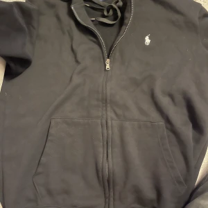 Svart hoodie från Ralph Lauren - Säljer en svart hoodie från Ralph Lauren med dragkedja och det klassiska logotypbroderiet på bröstet. Det är storlek L men passar mer M
