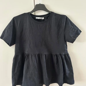 Svart kortärmad topp från Lager 157 - Säljer en svart kortärmad topp från lager 157 med en volangdetalj vid midjan. Toppen har en rund halsringning.