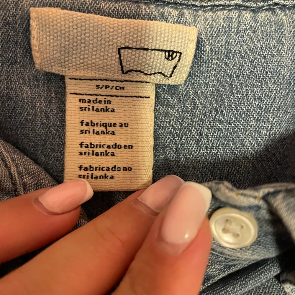 Säljer en klassisk blå jeansskjorta från Levi's med knappar framtill och två bröstfickor. Skjortan har långa ärmar och en stilren design som passar perfekt till vardags. Tillverkad i Sri Lanka.. Paidat.