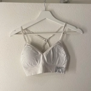 Vit linnetopp - Säljer en vit linnetopp  med smala axelband och korsad ryggdesign. Perfekt till träning eller som basplagg. Toppen har en enkel och stilren look.