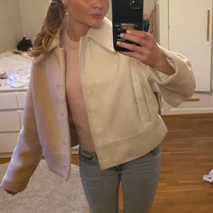 Vit kort kappa - Säljer en mysig vit jacka med knappar framtill. Jackan har en klassisk krage och långa ärmar, perfekt för kyligare vår dagar. Den är stilren och enkel att matcha med olika outfits. Nypris: runt 600-700
